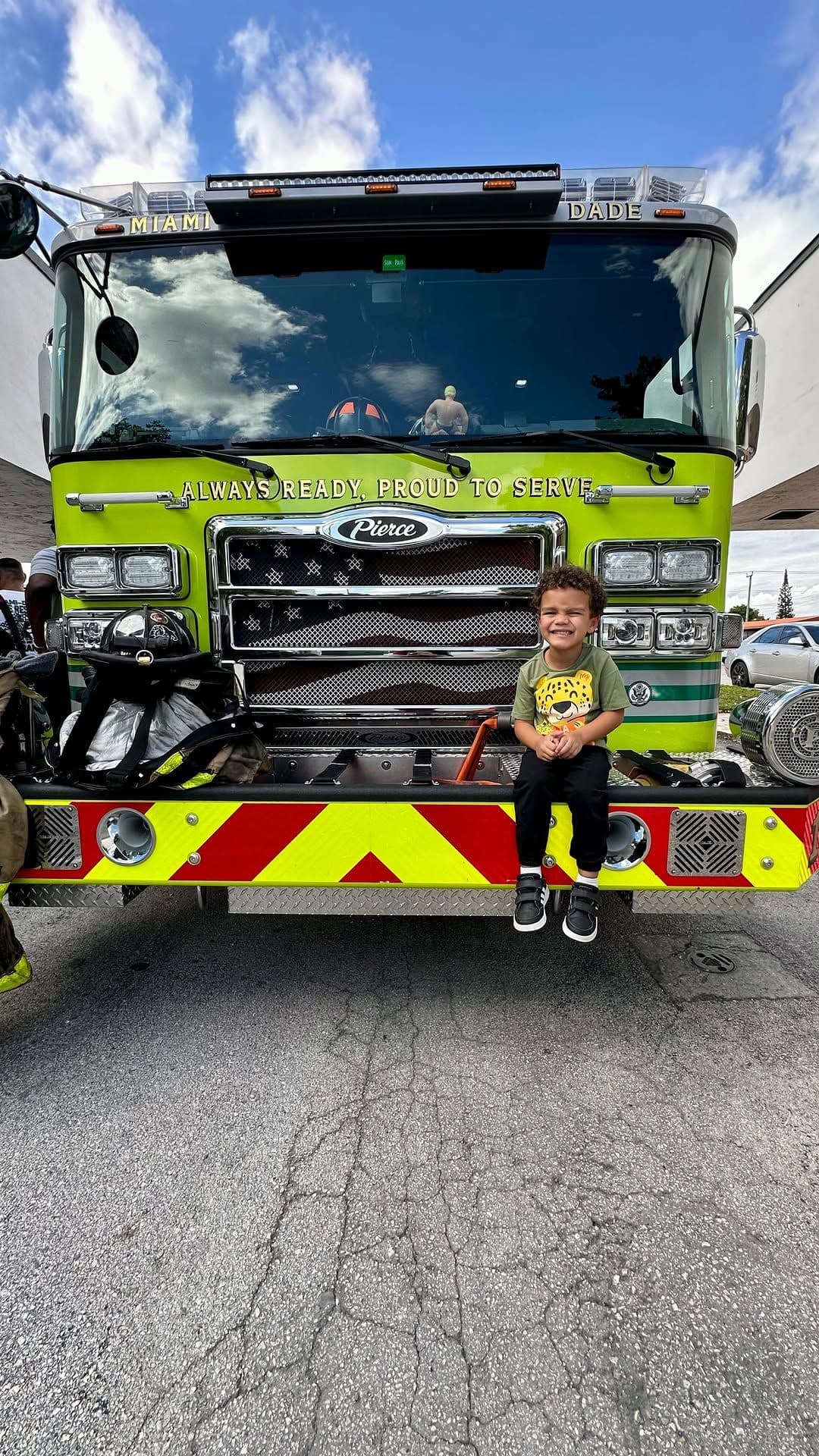 A student sitting on the bumper of a Miami-Dade Fire Rescue truck during a school visit.