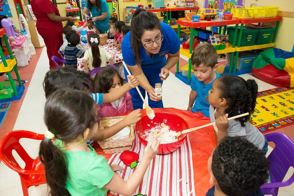 A teacher in the classroom leading a hands-on cooking project with preschoolers.